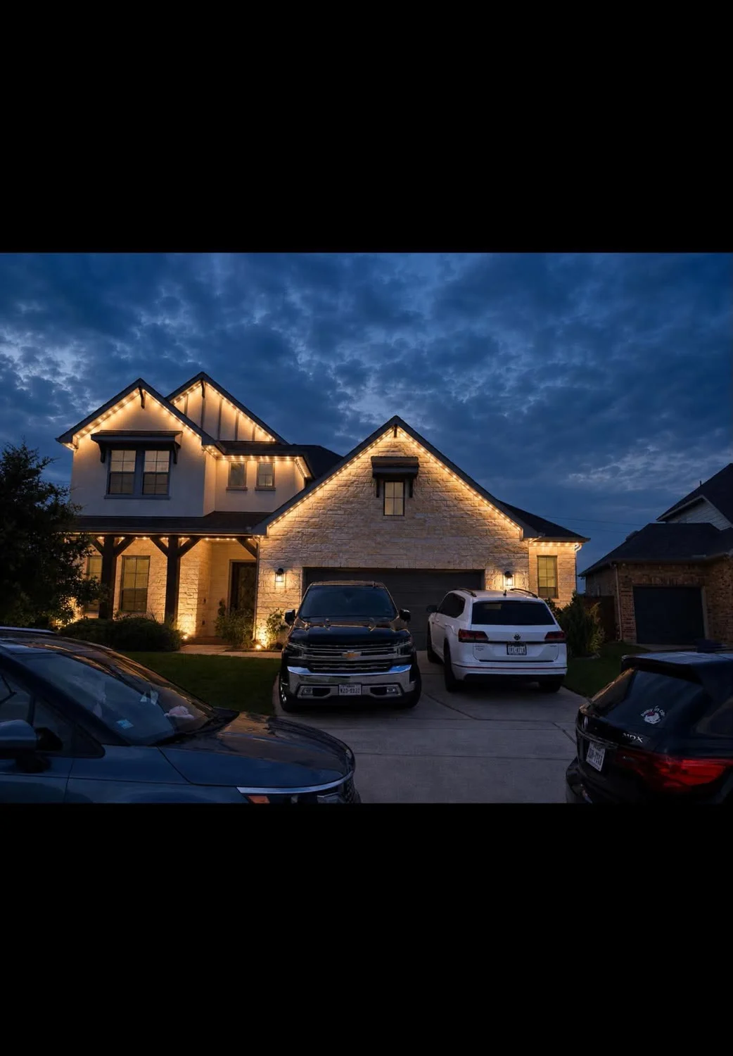 Real Skyclear install — warm-white permanent lighting outlining a two-story stone home at dusk